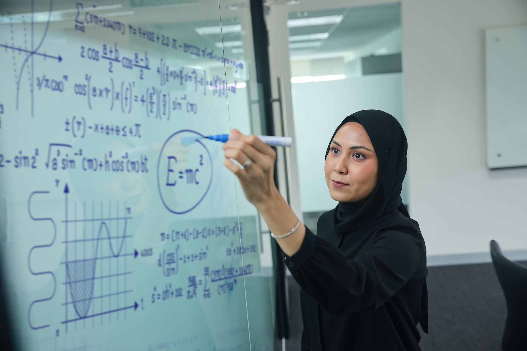 Young woman in modest dress writing equations on whiteboard