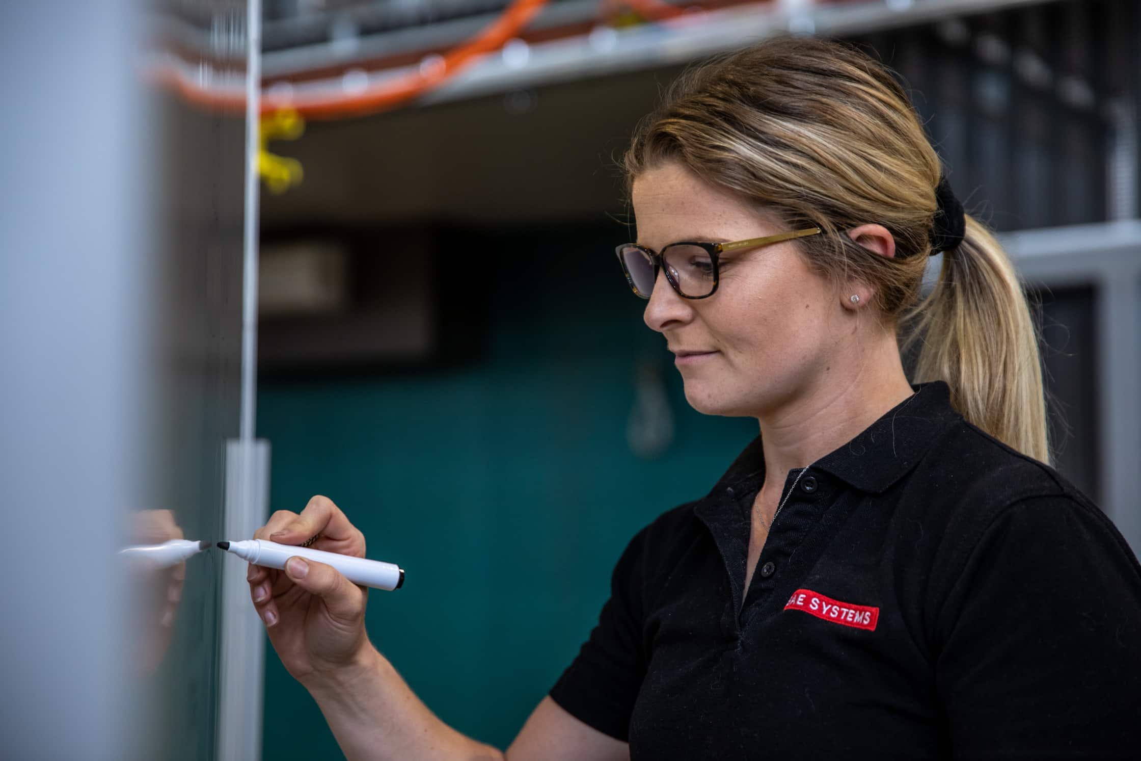 Employee in a BAE Systems monogrammed top writes on a whiteboard