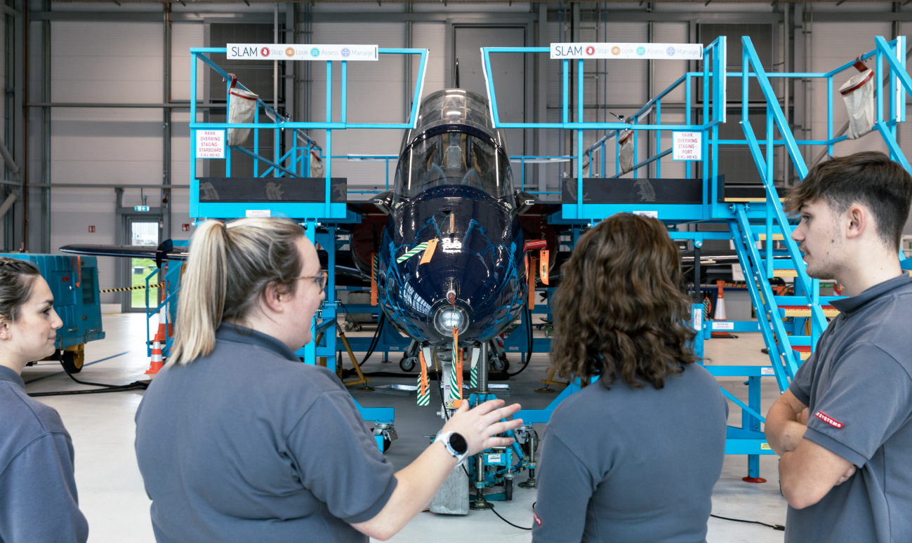 Four aeronautical engineers at BAE Systems hold a stand up meeting in front of an aircraft